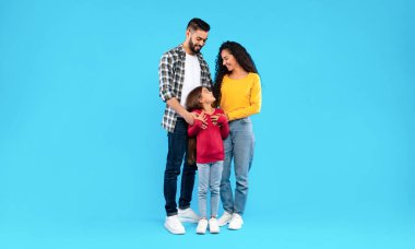 Orta Doğulu ebeveynler mutlu kızlarını kucaklıyor mavi arka planda bir arada duran sevimli çocuğa bakıyorlar. Neşeli Arap Aile Stüdyoda Sarılma Pozu Veriyor. Tam Uzunluk Görüntüsü