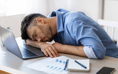 İşte uyu. Modern ofisin işyerinde çok çalışan yorgun bir adam laptopla ve raporlarla çalıştıktan sonra uyukluyor, masa başında oturuyor, baş aşağı oturuyor, iş yorgunluğu çekiyor.