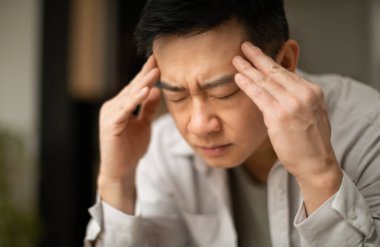 Orta yaşlı Asyalı adamın baş ağrısı çektiği, şakaklarına dokunduğu, gözleri kapalı oturduğu, fotokopi çektiği yakın plan. Migren, baş ağrısı, stres, gerilim sorunu, akşamdan kalma konsepti