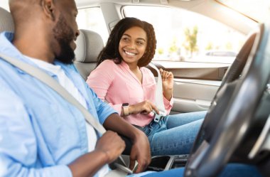 Önce güvenlik. Gülümseyen Afrikalı Amerikalı çift şehirde sürmeden önce emniyet kemerlerini bağlıyor, yeni lüks bir arabanın içinde oturuyor, güvenli sürüş kurallarını takip ediyor, otomobille seyahat etmeye hazır, birbirlerine bakıyor.