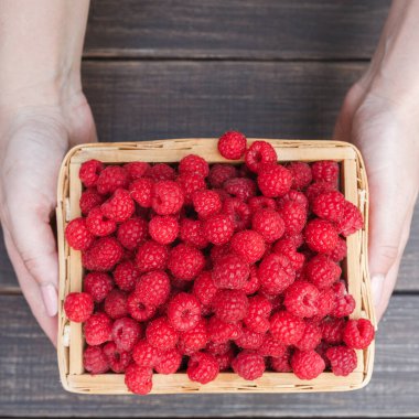 Kahverengi ahşap arka planda ahududu sepeti. Sağlıklı gıda konseptinin hasadı. Tahta masada doğal olgun organik böğürtlenler, üst manzara..