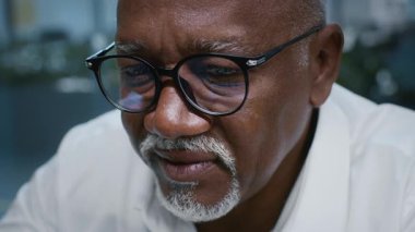 Gözlüklü, olgun bir Afrikalı Amerikalı, kurumsal ofis ortamında bir işe konsantre oluyor. İşiyle ilgilenirken ifadesi kararlılık ve profesyonelliği gösteriyor..