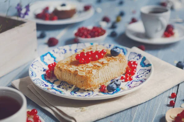 Böğürtlen, kırmızı frenk üzümü ve bluberries - pasta pasta ve çilek ile tatlı kahvaltı. Mavi rustik ahşap masada servis edilen güzel yemekler, etnik porselen tabakta kek tatlısı, çay ve kahve fincanı.