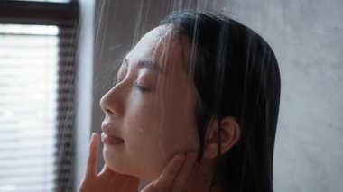 Genç bir Asyalı kadın şık banyosunda gençleştirici bir duş rutinine daldı. Huzurlu ortam, su taşarken kendi kendine bakım deneyimini arttırır ve rahatlık sağlar..