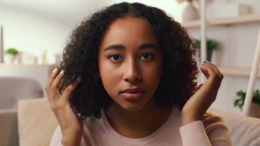 Güzel kıvırcık saçlı genç bir Afrikalı Amerikalı kadın evde dinleniyor. Kendine bakmakla meşgul, saçını düzeltiyor ve rahat bir ortamda yaşam tarzını benimsiyor..