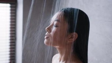 Genç bir Asyalı kadın şık bir banyoda duş alırken cilt bakımını alışkanlık haline getiriyor. Rahatlarken su onun üzerine dökülüyor, kişisel sağlığına odaklanıyor..