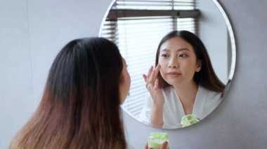 Genç bir kadın banyoda şımartma alıştırması yapıyor. Huzurlu ve rahatlatıcı bir atmosferin tadını çıkarırken cilt bakımı yapıyor. Mekan, huzurlu bir yaşam tarzı ve kişisel bakım alışkanlıklarını yansıtıyor..