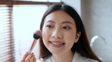 Genç bir Asyalı kadın banyoda kendi kendine bakım seansından zevk alıyor. Makyaj yapıyor ve şımarık bir yaşam tarzını benimsiyor. Nazikçe gülümsüyor, rahatlamış ve yenilenmiş rutinini gösteriyor..