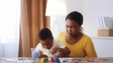 Annesi onu özenle ve sevgiyle izlerken, bir çocuk renkli resimlerle oynar, sanatına odaklanır. Sıcak yuvaları sıcak ve sevgi dolu bir atmosfer yaratıyor..