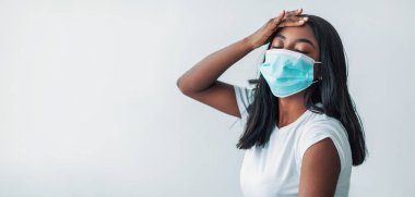 COVID-19 aşısının yan etkileri. Coronavirus antiviral iğnesinden sonra maskeli siyahi kadın koluna dokunan alnına, yüksek ateş, baş ağrısı, yüksek vücut ısısı...