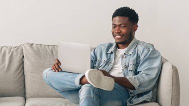 İnsanlar, Teknoloji ve Yaşam Tarzı Konsepti. Oturma odasındaki rahat koltukta oturan mutlu siyah çift portresi, cep telefonu tutan kadın, dizüstü bilgisayar kullanan adam. Wifi İnternet Bağlantısı