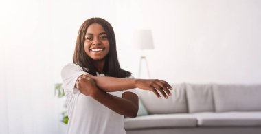 Heyecanlı genç Afrikalı Amerikalı çift kol kaslarını esnetiyor, evde ısınma egzersizleri yapıyor, kameraya bakarak poz veriyor. Milenyum siyahi erkek ve bayan ev içi eğitim alıyor, içeride çalışıyor.