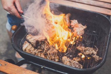 Metal ızgarada ateşte ızgara biftek. Şefin elleri bol ateşte kızartılmış et ızgarası pişiriyor. Barbekü taze et dilimleri..