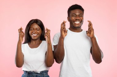 Afro-Amerikalı bir çift pembe bir duvara yaslanmış gülümserken parmaklarını çapraz yapıyorlar. Bir mucize ve iyi şeyler umuyorlar, pozitiflik ve beraberliği ifade ediyorlar..