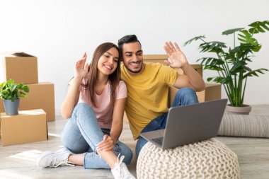 Mutlu bir çift gülümsüyor ve el sallıyor. Oturma odalarında içi taşınan kutular ve yeşil bitkilerle dolu bir video görüşmesi yapıyorlar. Rahat ve neşeli görünüyorlar..