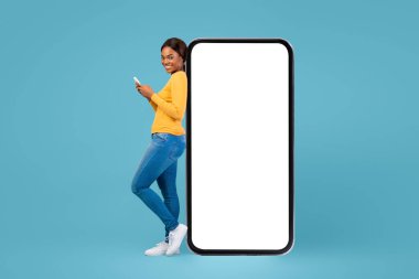 Genç bir kadın, yüzünde bir gülümseme olan akıllı telefonunu kullanarak büyük, boş bir ekranın yanında modern ve canlı bir atmosfer yaratıyor..