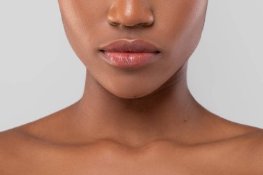 Kadının dudaklarının ve çenesinin doğal güzelliğini vurgulayan yakın çekimi. Pürüzsüz cilt genel görünüme zarafet ve berraklık ekler, düz bir arkaplan karşısında ayarlanır.