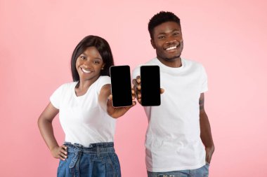 Neşeli siyah bir çift pembe bir stüdyoda, iki akıllı telefonu boş ekranlarla gururla sunuyorlar. Yaratıcı kullanım araçlarını sergilemek için heyecanlılar..