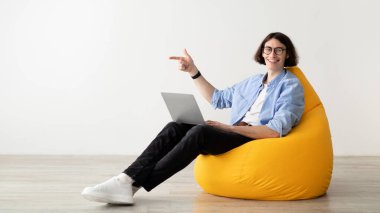 Genç bir adam parlak sarı bir fasulye çuvalında dizüstü bilgisayarıyla rahatça oturuyor. Neşeli bir şekilde gülümseyerek şık bir kapalı mekan ortamında rahat bir anın tadını çıkarıyor..