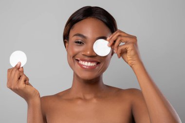 Genç bir kadın bir gözüne pamuk tutarken diğerini de elinde sallıyor. Neşeli bir ifadesi var. Kusursuz cildini ve cilt bakımının heyecanını vurguluyor..