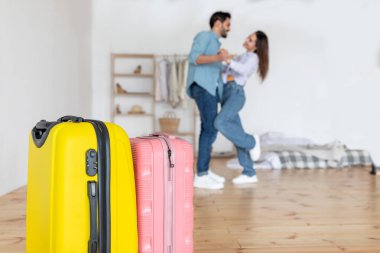 Mutlu bir çift samimi bir odada birbirine yakın dans eder. Ön plandaki renkli bavullar bir yolculuğa başladıklarını gösteriyor. Sıcak bir atmosfer onları sarıyor..