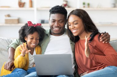 Üç kişilik neşeli bir aile evdeki rahat bir kanepede dizüstü bilgisayarla meşgul oluyorlar. Anne ve baba gülümserken çocuk ekranda el sallıyor ve sıcak bir ortam yaratıyor..