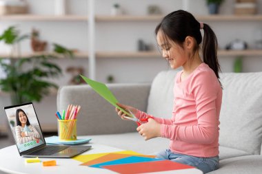 Bir kız renkli kağıtları keserken gülümserken bir yandan da bir arkadaşını laptoptan arıyor. Oda pırıl pırıl ve davetkar. Malzemeler düzgün düzenlenmiş..