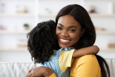 Neşeli bir anne kızını sıcak bir oturma odasına yakın tutar. Gülüşleri sevgi ve mutluluğu yansıtıyor. Yürek ısıtan bir aile sahnesi yaratıyor..