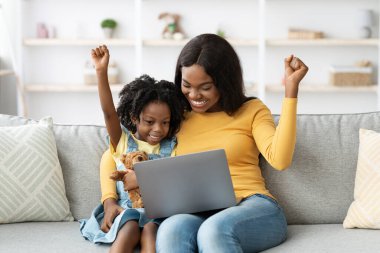 Genç bir kız annesinin yanında kanepede otururken sevinçle tezahürat yapar. Anne dizüstü bilgisayarla meşgulken gülümsüyor ve evlerinde mutlu bir anı paylaşıyor..