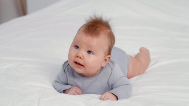 Neşeli bir bebek, evde yumuşak bir battaniyeyle karnını keşfediyor. Güneş ışığı odayı nazikçe aydınlatıyor, aile ile paylaşılan neşe ve şefkat anlarını vurguluyor..