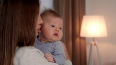 Bir anne sevgiyle yeni doğan bebeğini sıcak ve davetkar bir yuvaya yatırır. Lambanın yumuşak parıltısı, samimi atmosfere eklenir. Bağlarını ve sevgilerini gösterir..