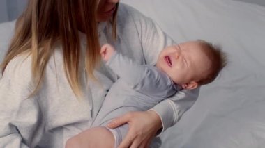 Bir anne ağlayan bebeğini sıcak bir evde nazikçe kucağına alır. Yeni doğmuş gibi görünen çocuk, sıkıntı belirtileri gösteriyor. Sıcak atmosfer bağlarını vurgular..