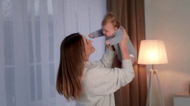 Neşeli bir anne neşeli bebeğini havaya kaldırır, sıcak, aydınlık bir odada sevgisini gösterir. Bebek kıkırdıyor, yürek ısıtan bir atmosfer yaratıyor..