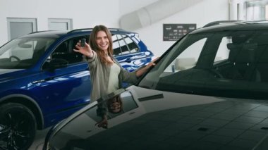 Modern arabalarla dolu bir araba galerisinde parlak siyah bir aracı keşfederken bin yıllık bir kadın sevinçle el kol hareketi yapıyor. Havalı SUV 'lerle çevrili kiralama seçenekleri konusunda hevesli görünüyor..