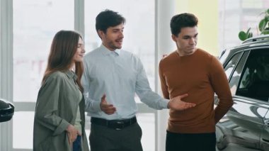 Bir araba satış temsilcisi, parlak bir otomobil salonundaki bir çiftle, araç seçeneklerini tartışarak etkileşime geçer..