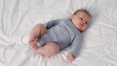 Açık renk saçlı rahat bir bebek evdeki rahat beyaz bir battaniyenin üzerinde rahatça yatar. Huzurlu atmosfer harika bir aile sevgi ve bakım anını yansıtıyor..