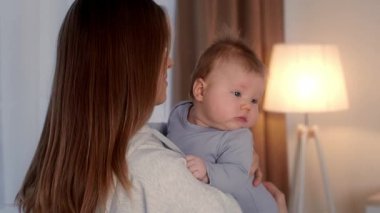 Şefkatli bir anne bebeğini sıcak, sıcak bir ev ortamında kucaklar. Yumuşak ışıklandırma, özel bir bağı paylaştıkça sevgi dolu anı güçlendirir..
