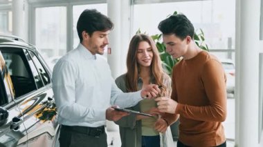 Modern bir araba galerisinde iki bin yıllık bir satış elemanı bir araç satın alma ya da kiralama seçeneklerini tartışıyor. Atmosfer profesyonel ve misafirperver..