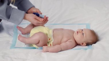 Sevgi dolu bir bakıcı sıcak bir ev ortamında bebek bezini nazikçe değiştirir. Sarı bir bebek bezi giyen çocuk, yumuşak bir battaniyeye uzanıp, hassas bir an sergiliyor..