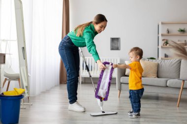 Bir anne ve küçük oğlu zemini birlikte temizliyorlar. Anne, çocuk temiz bir bez tutarken nasıl paspas kullanılacağını gösterir..