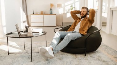 Genç bir adam, kulaklık takmış ve müzik dinlemekten zevk alan bir fasulye çuvalında rahatça oturuyor. İyi aydınlatılmış, şık bir odada, yakınlardaki bir masada bir dizüstü bilgisayar duruyor..