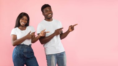 Mutlu siyah bir çift pembe bir stüdyoda yan tarafı göstererek birlikte duruyorlar. Seyircileri, neşeli ifadeleri ve jestleriyle bir teklif veya fırsat değerlendirmeye davet ediyorlar..