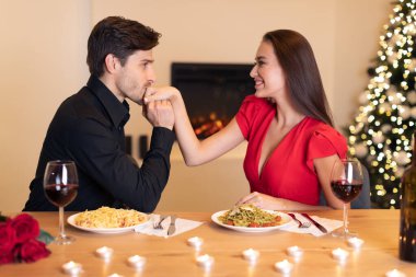 Romantik bir akşam yemeği sırasında mumlar ve şenlikli bir atmosferle çevrili bir çift samimi bir anı paylaşıyor. Erkek, makarna ve şaraptan hoşlanan kadınların elini nazikçe öper..