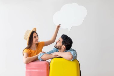 Bir adam ve bir kadın parlak renkli bavulların yanında durur ve kadın kafasının üstünde bir konuşma balonu tutarken eğlenceli bir şekilde seyahat planlarını tartışırlar..