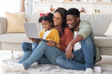 Mutlu bir aile, parlak oturma odalarının zemininde dizüstü bilgisayarla yakından ilgilenir. Gülüşleri ve kahkahaları paylaşıyorlar, birlikte neşeli anlar yaratıyorlar..