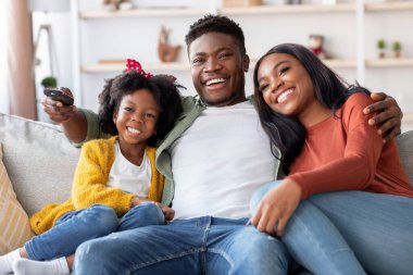 Üç kişilik bir aile rahat bir kanepede oturup film gecesinin tadını çıkarıyor. Gülüşleri ve kahkahaları uzaktan kumandayla paylaşıyorlar..