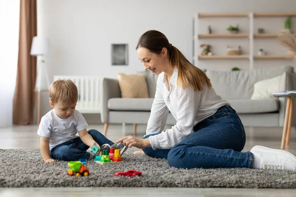 Genç bir çocuk yumuşak bir halıya oturur, renkli bloklarla inşa etmeye odaklanır. Bu sırada annesi ona yardımcı olur, keyifli oturma odalarında besleyici bir ortam yaratır..