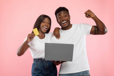 Mutlu bir siyah çift dizüstü bilgisayar ve kredi kartıyla birlikte online alışveriş deneyimlerini kutluyor. Eğlenirken neşeli ve dışavurumludurlar..