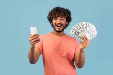 Doğulu neşeli bir genç bir adam bir elinde cep telefonu, diğer elinde de yüklü miktarda para ile poz veriyor..
