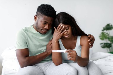 Genç çift bir yatağa yakın otururlar, yüzlerindeki ifade endişe ve endişeyi yansıtır..